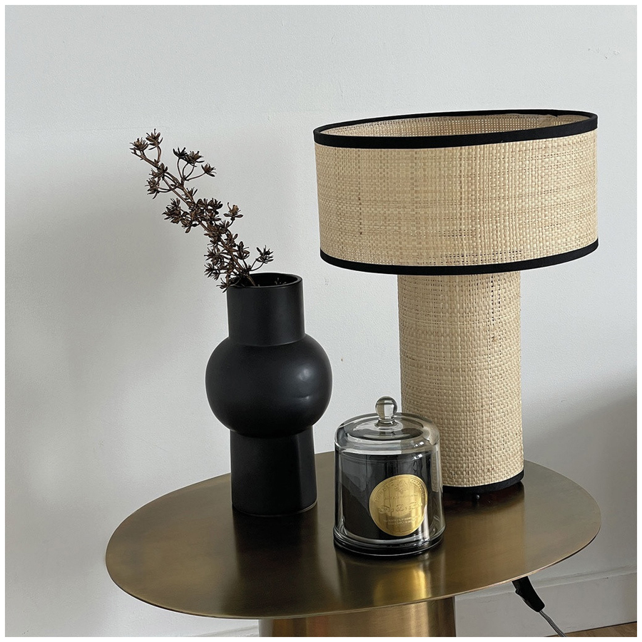 Bougie noire Feu de Bois sous cloche en verre, disposée sur une table dorée avec lampe en rotin et vase décoratif - Dakar, Sénégal.