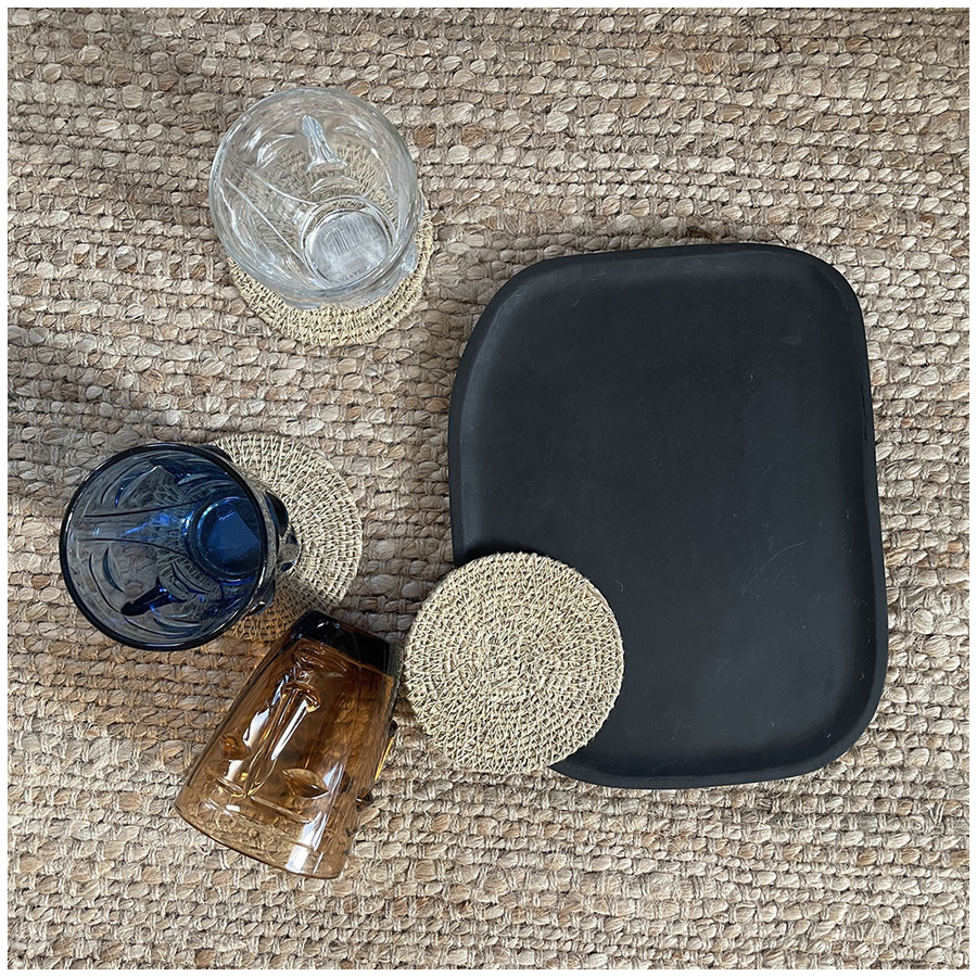 Plateau Osmose ovale en bois noir présenté avec des verres colorés et des dessous de verre sur une surface texturée - Dakar, Sénégal