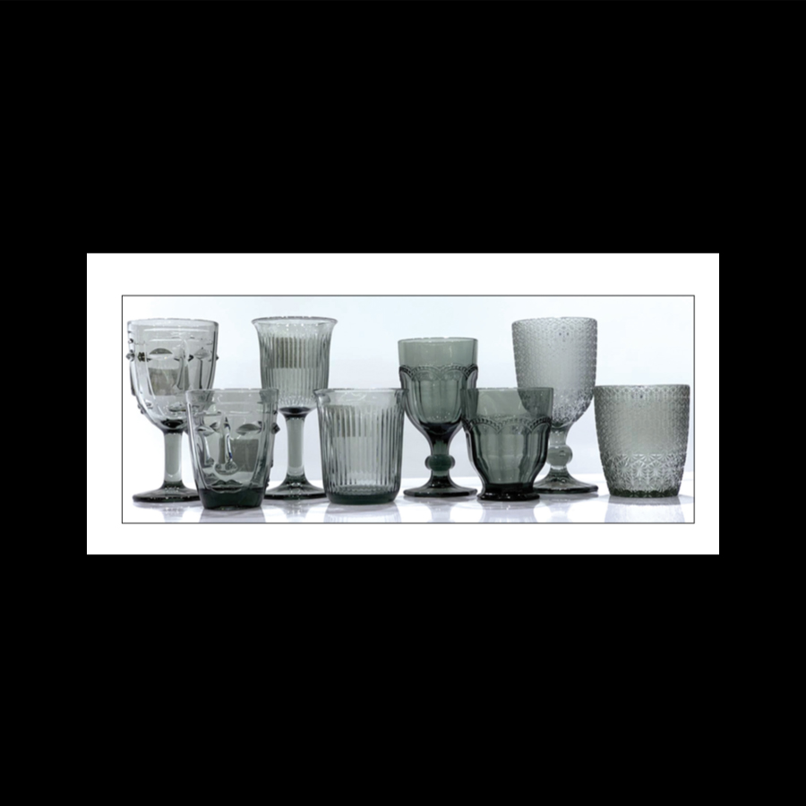 Collection de coupes et verres en verre gris de styles variés, y comprenant une coupe à pied Visage, présentées alignées sur une étagère à Dakar, Sénégal.