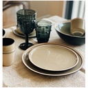 Assiette plate Wabi en grès sable, intégrée dans une table dressée avec des verres en verre teinté pour une ambiance conviviale - Dakar, Sénégal