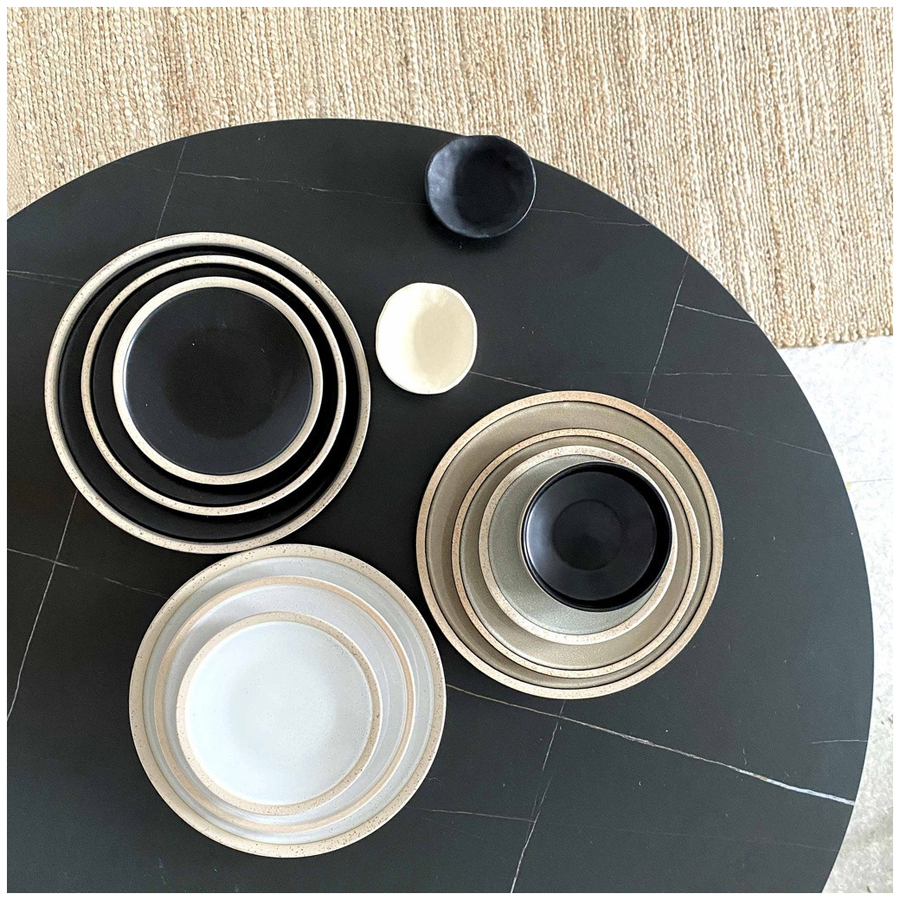 Collection Wabi en grès sable, comprenant des assiettes plates et des coupelles, présentée sur une table moderne - Dakar, Sénégal