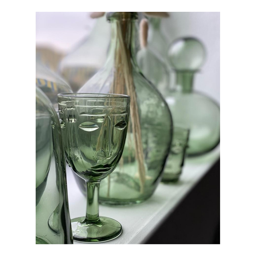 Verres à pied en verre vert et carafes assorties posés sur une surface beige, design artistique. Dakar, Sénégal."