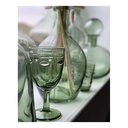 Verres à pied en verre vert et carafes assorties posés sur une surface beige, design artistique. Dakar, Sénégal."